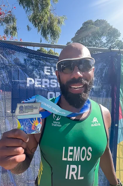 Leo in a green Ireland race kit marked LEMOS IRL, holding his World Triathlon medal in Townsville
